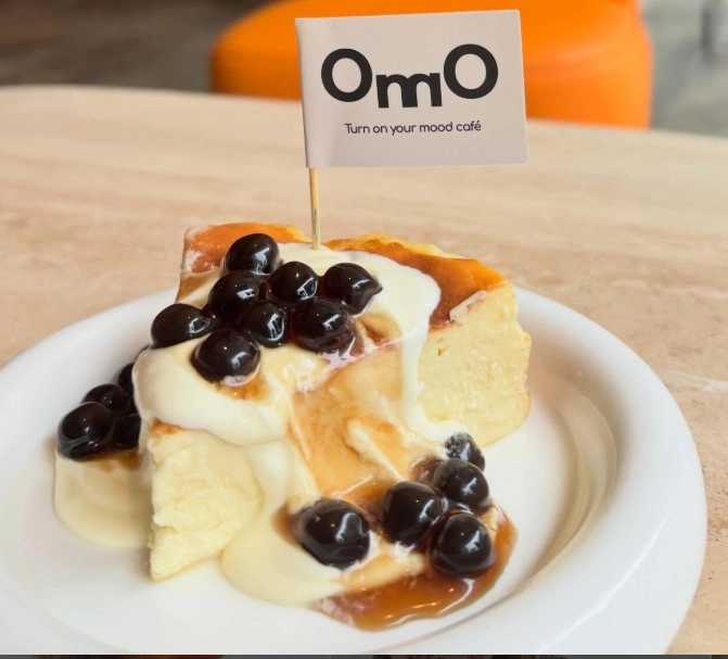 OmO Cafe 歐莫瀑布珍珠巴斯克，插有 OmO 品牌小旗子的綿密乳酪蛋糕，流淌滑順鮮奶油與晶瑩珍珠