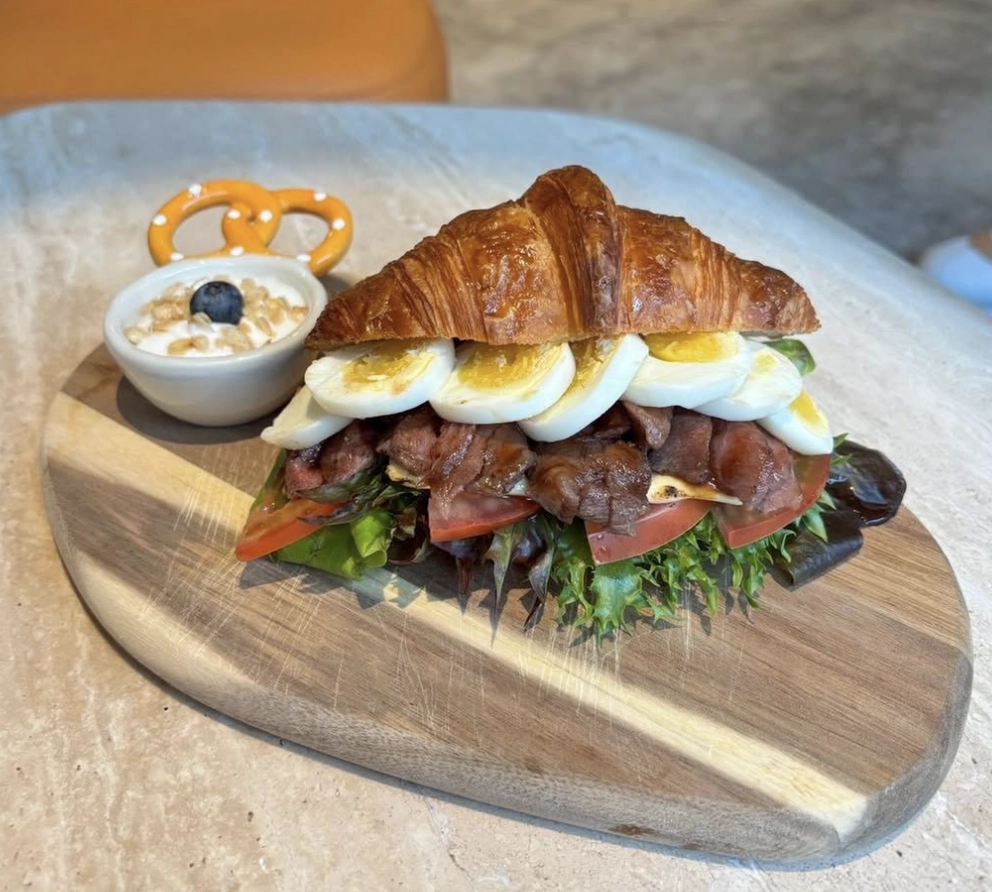 OmO Cafe 歐莫牛肉可頌三明治木盤特寫，內餡有新鮮生菜、番茄片、炙燒牛肉與水煮蛋