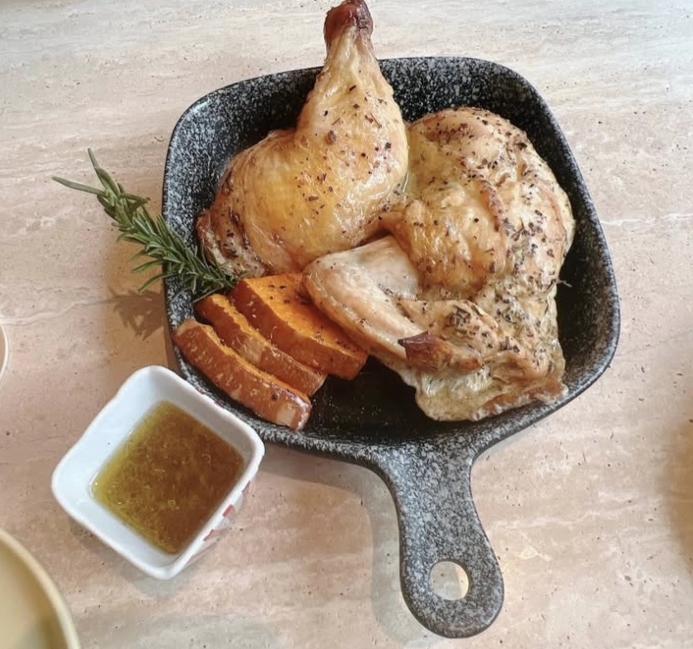 OmO Cafe 歐莫烤半雞鐵鍋特寫，表面撒滿迷迭香料的微焦脆皮大雞腿，附南瓜片與沾醬
